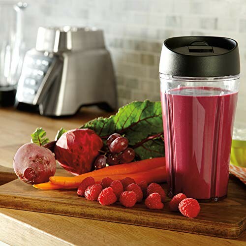 A smoothie in a glass with fresh raspberries, grapes, beet, and carrots on a wooden board.